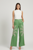 Woman wearing green pants with leaf patterns and a white top on a white background